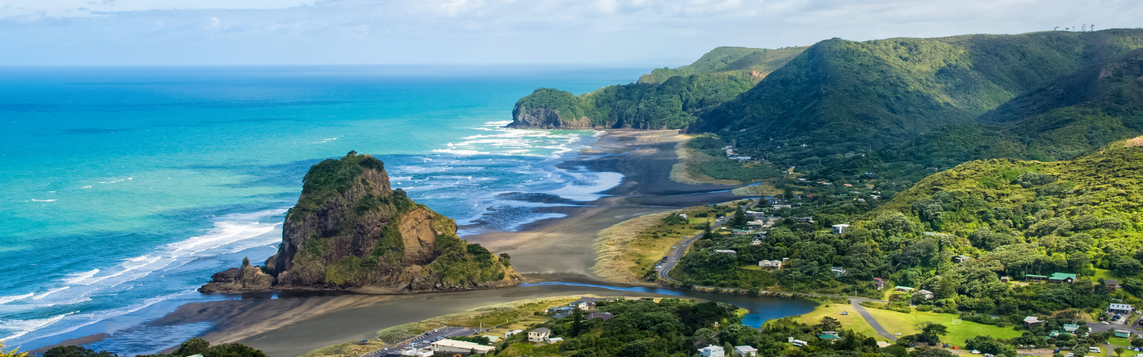 Turquoise waves meet tall green hills, with a sandy beach separating them. 